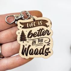 a hand holding a wooden keychain that says life is better in the woods