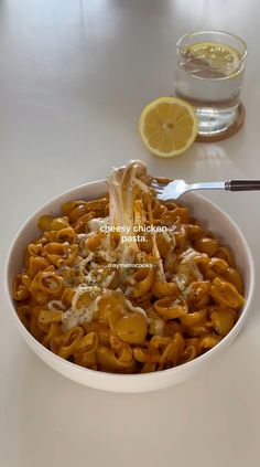 a white bowl filled with pasta and sauce next to a glass of lemonade on a table