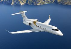 an airplane flying over the ocean with mountains in the backgrounnd and blue water behind it