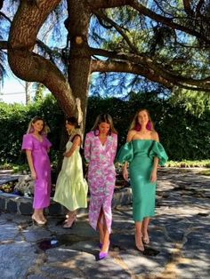 three women in colorful dresses are standing under a tree with their hands on their hips