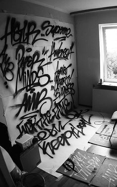 black and white photograph of graffiti on the wall in an unfinished room with a window