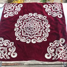 a red blanket with white designs on it sitting on top of a wooden table next to chairs