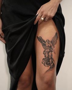 a woman's thigh with an angel tattoo on her left leg and a black skirt underneath