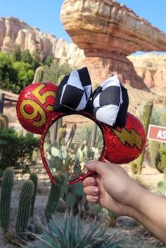 a hand holding up a mickey mouse ears headband in front of some cactus plants