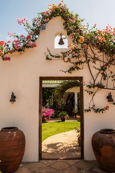 an open door to a white building with flowers on the wall and potted plants