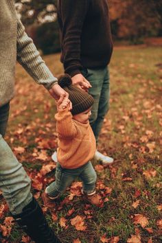 a man holding the hand of a little boy who is wearing a brown sweater and hat