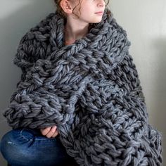 a woman sitting on the floor wrapped in a gray knitted shawl, looking off to the side