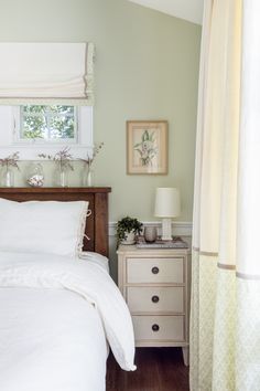 a white bed sitting in a bedroom next to a window with curtains on the windowsill