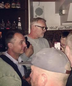 a group of men standing next to each other in a bar talking on cell phones