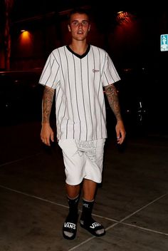 a man with tattoos and white shorts is standing in the parking lot wearing black shoes