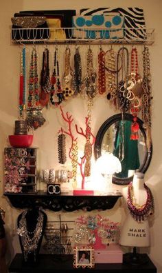 a shelf filled with lots of jewelry next to a wall mounted necklace holder and mirror