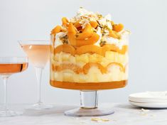 an orange and white layered cake next to two wine glasses