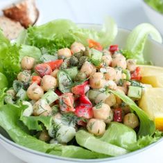 a salad with chickpeas, tomatoes and lettuce in a white bowl