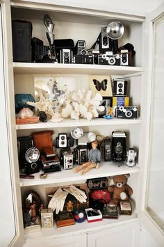 a white book shelf filled with lots of different types of cameras and other things on top of it