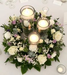 candles are lit in the center of a floral arrangement on a white tablecloth with flowers and greenery