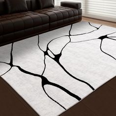 a living room area rug with black and white designs on it's floor, in front of a brown leather couch