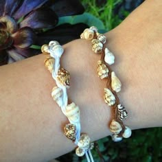 two bracelets with seashells on them sitting on a woman's arm