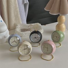 four clocks sitting on top of a table next to a lamp