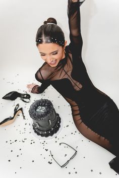 a woman in a black dress sitting on the floor next to a cake and scissors