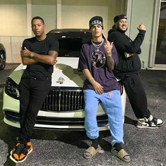 two young men sitting on the hood of a white car in front of a building