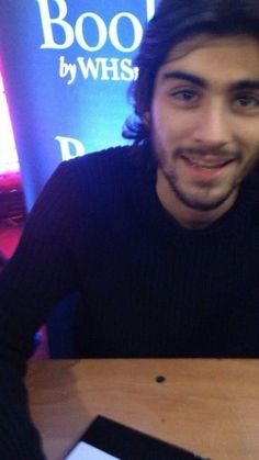 a man sitting at a table with a pizza in front of him and smiling for the camera