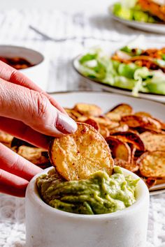 a person dipping guacamole into a small bowl with chips on the side