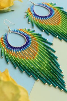 two pairs of colorful beaded earrings sitting on top of a table next to yellow flowers