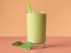 a green smoothie in a tall glass with a straw on the side and a leaf sticking out of it