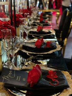 the table is set with black and gold place settings, red roses on each plate