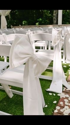 a row of white chairs with bows tied to them on the grass at a wedding