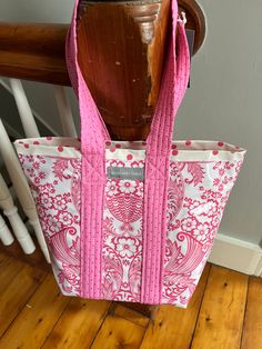 a pink and white tote bag sitting on top of a wooden chair next to a wall