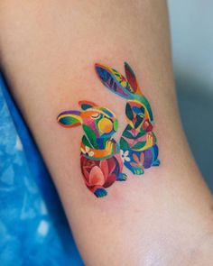 a colorful tattoo on the arm of a woman's leg with two rabbits painted on it