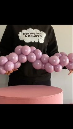 a person is holding some balloons in front of a pink stool with the word balloon art on it