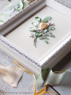 a white box with flowers on it and ribbons around the edges, sitting on a table