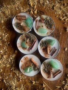 four white dishes filled with food sitting on top of a wooden table covered in dirt