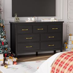 a christmas tree is in front of a flat screen tv on a dresser next to a bed