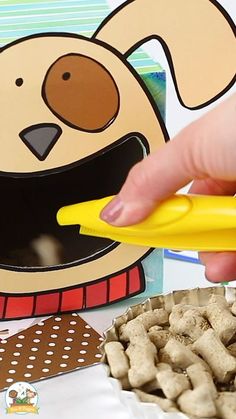 a person is holding a yellow object near some dog food and a paper cutout