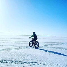 a person riding a bike in the snow on a sunny day with blue skies and no clouds