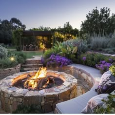 an outdoor fire pit surrounded by plants and flowers