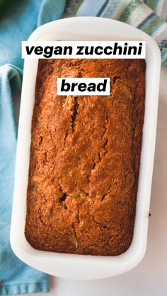 a loaf of zucchini bread in a white dish on a blue towel next to an avocado