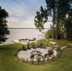 a fire pit in the middle of a grassy area next to a body of water