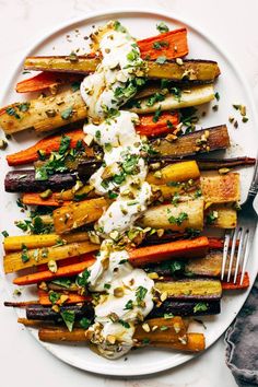 a white plate topped with carrots covered in sour cream and garnished with herbs