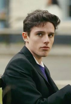 a man in a suit sitting on a bench with his arms crossed and looking at the camera