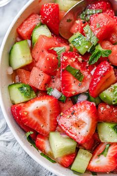 a white bowl filled with sliced strawberries and cucumber on top of a table