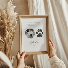 a woman holding up a framed photo with two dogs paw prints in front of her