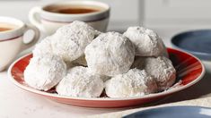 powdered sugar covered donuts on a red plate next to cups of coffee and saucers