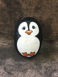 a painted rock with a small penguin on it's face, sitting in front of a stone wall