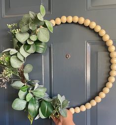 a hand holding a wooden beaded wreath with greenery on the front and side