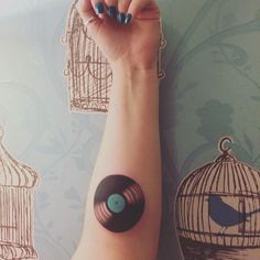 a woman's arm with a vinyl record on it and birdcage in the background