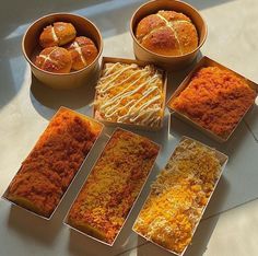 six different types of baked goods in boxes on a white counter top with bowls and spoons